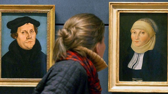 Eine Frau betrachtet zwei Cranach-Gemälde, die Martin Luther und seine Frau Katharina von Bora zeigen. © dpa/dpaweb Foto: Waltraud Grubitzsch