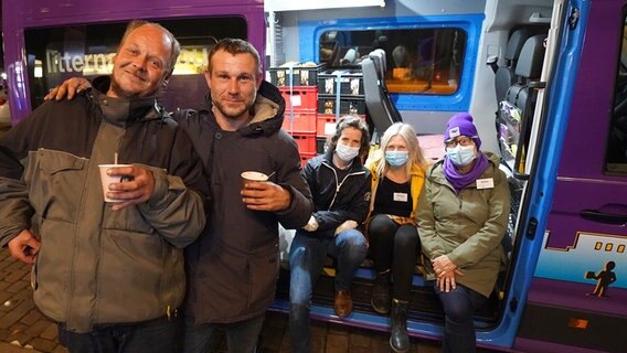 Zwei obdachlose Männer stehen mit ihren Heißgetränken vor dem Mitternachtsbus, in dem die ehrenamtlichen Helferin Anne (r), Sonja Norgall (2.v.r), Projektleiterin Mitternachtsbus für obdachlose Menschen, und die ehrenamtliche Helferin Berit (3.v.r) sitzen. © picture alliance/dpa Foto: Marcus Brandt