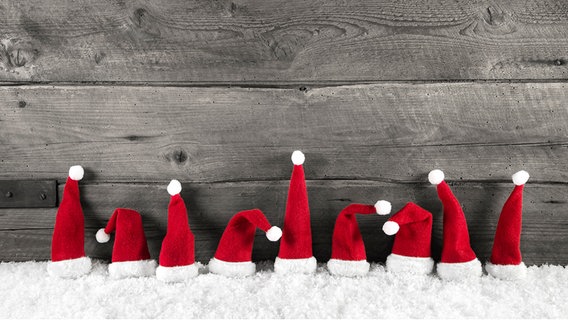 Weihnachtsmützen auf Kunstschnee vor einer Holzwand © Fotolia Foto: Jeanette Dietl