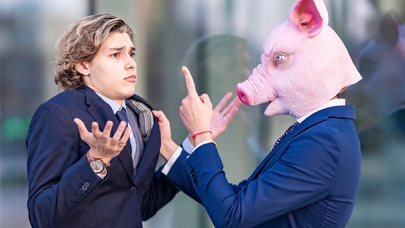 Mann mit Schweinemaske zeigt auf Kollegen, der mit den Schultern zuckt. © picture alliance / Westend61 | GER 