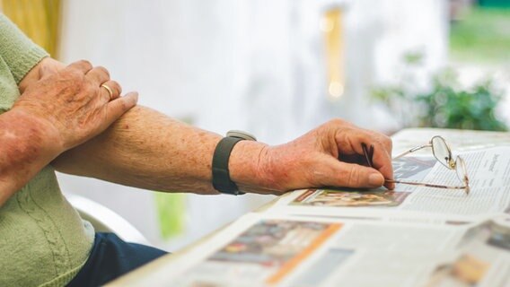 Eine Senioren sitzt an einem Tisch auf dem eine ausgebreitete Zeitung liegt © photocase Foto: poly picture