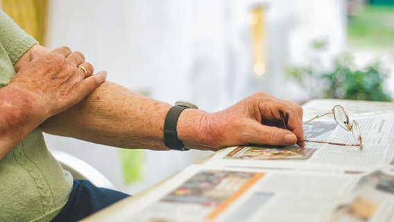 Eine Seniorin sitzt an einem Tisch,auf dem eine ausgebreitete Zeitung liegt. © photocase Foto: poly picture