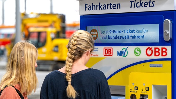Zwei junge Frauen stehen am Hauptbahnhof in München an einem Fahrkartenautomaten auf dem Werbung für das 9-Euro-Ticket zu sehen ist. © picture alliance/dpa Foto: Lennart Preiss