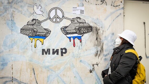 Eine Frau betrachtet in Rom ein Bild der Straßenkünstlerin Laika. Es zeigt zwei Panzer, die Friedensymbol formen. © picture alliance / ZUMAPRESS.com Foto: Marilla Sicilia