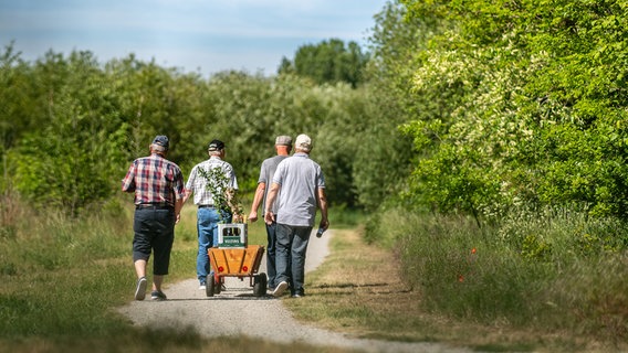 Vier Männer gehen am Vatertag mit einem Bollerwagen, auf dem zwei Kisten Bier stehen, einen Weg entlang. © picture alliance/dpa Foto: Guido Kirchner