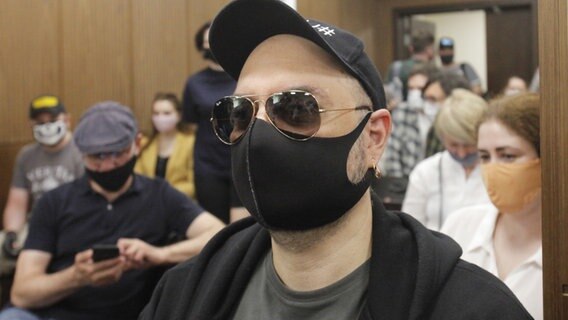 Kirill Serebrennikow sitzt mit schwarzer Sonnenbrille, Schirmmütze und Mundschutz im Gerichtssaal. © picture alliance/Uncredited/AP/dpa 