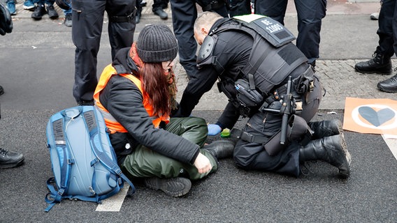 Eine junge Frau mit Warnweste sitzt auf dem Boden. Hinter ihr kniet ein Polizist. © picture alliance Foto: Geisler-Fotopress