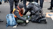 Eine junge Frau mit Warnweste sitzt auf dem Boden. Hinter ihr kniet ein Polizist. © picture alliance Foto: Geisler-Fotopress