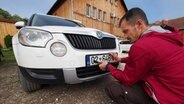 Ein Mann nimmt das Nummernschild seines Autos ab, damit das Auto in serbischen Gebieten nicht beschädigt wird. © pd-bild Klaus Honigschnabel 