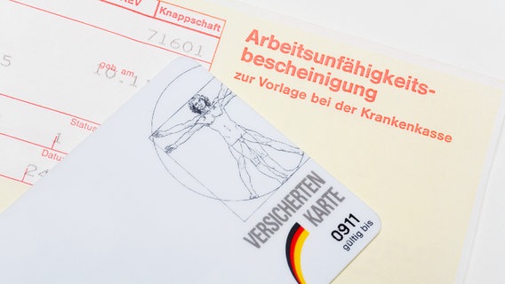 Eine Arbeitsunfähigkeitsbescheinigung und eine Versichertenkarte. © picture alliance / VisualEyze 