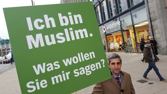 Michel Abdollahi mit einem Schild, auf dem steht: Ich bin Muslim. Was wollen Sie mir sagen? © NDR / Stefan Mühlenhoff 