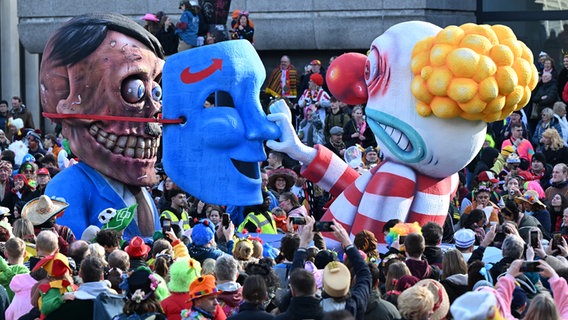 Ein Mottowagen, der einen entsetzten Clown zeigt, der hinter einer AfD-Maske den noch lebenden Hitler entdeckt, fährt im Rosenmontagszug durch eine Menschenmenge feiernder Karnevalisten. © picture alliance/dpa | Federico Gambarini 