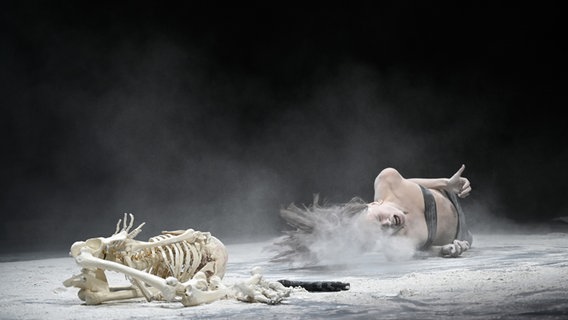 Eine Frau liegt auf einer Bühne neben einem Skelett. © Thomas Aurin 