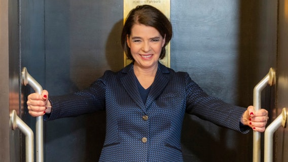 Susanne Daubner steht in einem Paternoster und lächelt in die Kamera. © HR/ARD/Thomas Ernst 