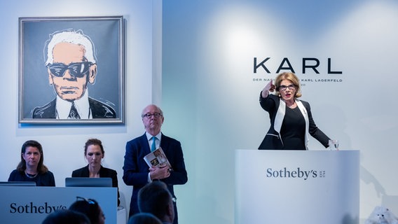 Die Auktionatorin Carline Lang steht bei der Auktion von Karl Lagerfelds Nachlass vor den Bietern in einem großen Raum. © dpa-Bildfunk Foto: Rolf Vennenbernd
