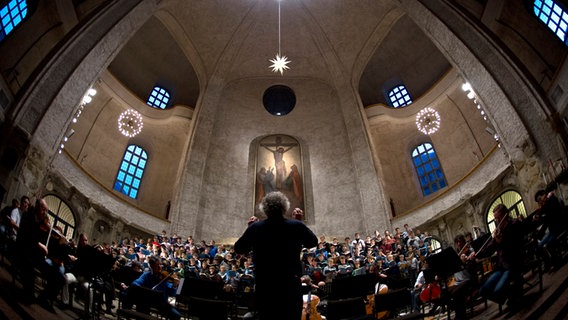 Ein Dirigent steht vor einem Orchester in einer Kirche. © picture alliance / dpa | Arno Burgi 