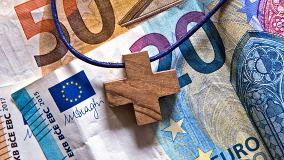Eine Kette mit einem Kreuzanhänger liegt auf Euro-Banknoten © picture alliance / epd-bild Foto: Heike Lyding