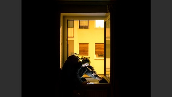 Eine Fotografie zeigt eine junge Frau, die auf einem Fensterbrett sitzt und auf ihr Handy tippt. © Valentin Goppel 