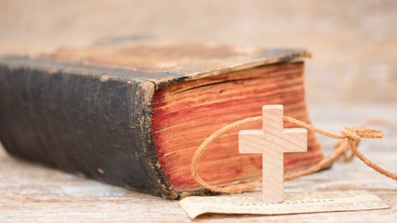 Eine Bibel liegt auf dem Tisch, davor ein kleines Holzkreuz © Fotolia 
