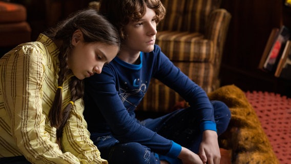 Szenenbild aus "The Black Phone": Ein Junge und ein Mädchen sitzen in einem Wohnzimmer, sie lehnt ihren Kopf an seine Schulter. © dpa-Bildfunk 