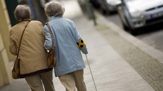 Eine Begleiterin führt eine blinde Frau mit einer Blindenbinde auf einem Fußweg © picture-alliance/ ZB Foto: Arno Burgi