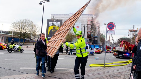 Un pompier et plusieurs assistants transportent un tableau à travers une rue.  © photo alliance Photo : Ida Marie Odgaard