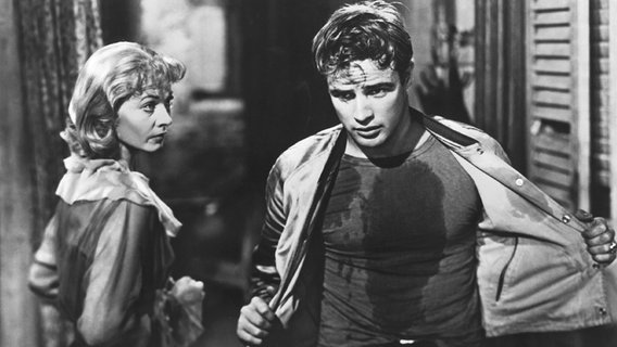 Eine Frau (Vivien Leigh) blickt einen Mann (Marlon Brando) an, der in verschwitzter Kleidung neben ihr steht. © picture-alliance 