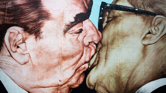 Graffiti shows the brotherly kiss between Leonid Brezhnev and Erich Honecker, artist Dimitrij Vrubel, on display in the East Side Gallery, Berlin.  © picture alliance / imageBROKER Photo: Mara Brandl