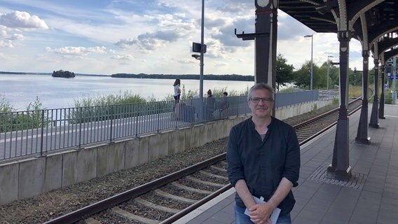 Autor Christopher Ecker am Bahngleis des Bahnhofs Plön mit dem Großen Plöner See im Hintergrund. Autor Christopher Ecker am Bahngleis des Bahnhofs Plön mit dem Großen Plöner See im Hintergrund. Foto: Anina Pommerenke