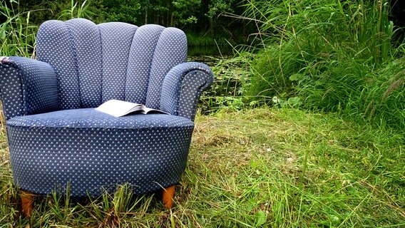 Ein Buch liegt aufgeschlagen auf einem Sessel, der auf einer Wiese steht. © Fotolia Foto: liabella13