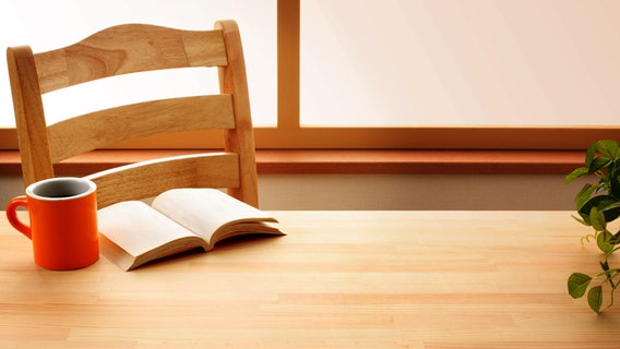 Ein Buch liegt aufgeschlagen auf einem Tisch neben einem Kaffeebecher. © Fotolia Foto: horiyan