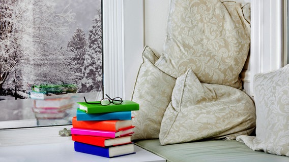 Ein Bücherstapel mit Lesebrille darauf liegt auf einer Fensterbank. © iStock Foto: Jo Ann Snover