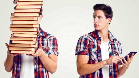 Ein junger Mann trägt einen Bücherstapel. Ein weiterer hält ein Smartphone in der Hand und sieht den ersten kritisch an. © fotolia.com Foto:  Tijana