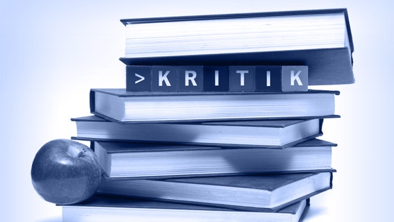 Ein blau anmutender Buchstapel mit Würfel die das Wort "Kritik" ergeben. © fotolia.com Foto: Matthew Benoit