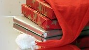 Auf einem Stapel weihnachtlich eingepackter Bücher liegt eine Weihnachtsmann-Mütze. © picture-alliance / Lehtikuva 