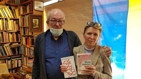 Ein Paar steht in einem Buchladen vor einer ukrainischen Flagge. © NDR Foto: Petra Volquardsen