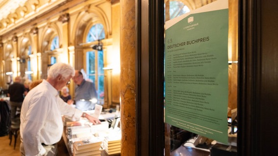 Ein Mann, verschwommen durch einen Türausschnitt zu sehen, stöbert in einer Bücherkiste. © Literaturhaus Hamburg Foto: Daniel Müller