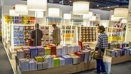 Eine Frau und zwei Männer betrachten die Bücherauswahl an Regalen voller Bücher und auf Stapeln - Bild auf der Buchmesse Frankfurt © imago/Rupert Oberhäuser Foto: Rupert Oberhäuser