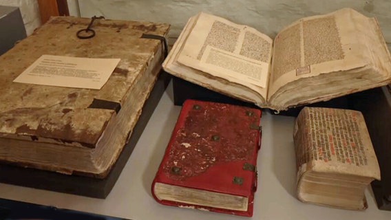 Mehrere alte Bücher liegen geschlossen und aufgeschlagen in einer Vitrine. © NDR.de 