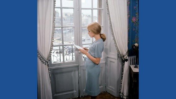 Catherine Deneuve steht am Fenster und liest einen Brief - Szene aus dem Film "Les Parapluies de Cherbourg" (Die Regenschirme von Cherbourg), 1964 © Ciné Tamaris / courtesy Schirmer/Mosel Foto: Léo Weisse