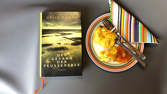 Das Buch "Der Gesang der Flusskrebse" von Delia Owens liegt neben einem Teler mit einer Kartoffelspeise.  