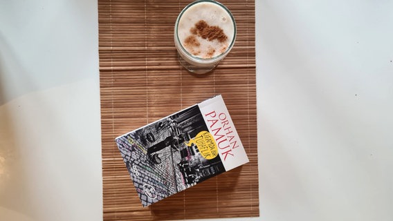 Ein Buch von Orhan Pamuk steht neben einem Glas türkischem Boza mit Zimt bestreut - Bild zum Podcast eat READ sleep Folge 28 Türkisches Boza mit David Safier Ein Buch von Orhan Pamuk steht neben einem Glas türkischem Boza mit Zimt bestreut - Bild zum Podcast eat READ sleep Folge 28 Türkisches Boza mit David Safier © NDR Foto: Jan Ehler