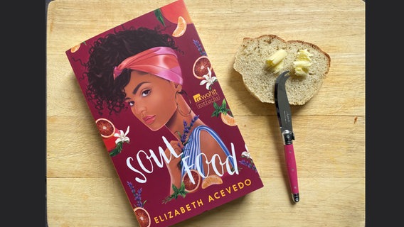 Elizabeth Acevedos Buch "Soul Food" neben einer Scheibe Bierbrot mit Butter und einem Messer © NDR Foto: Katharina Mahrenholtz