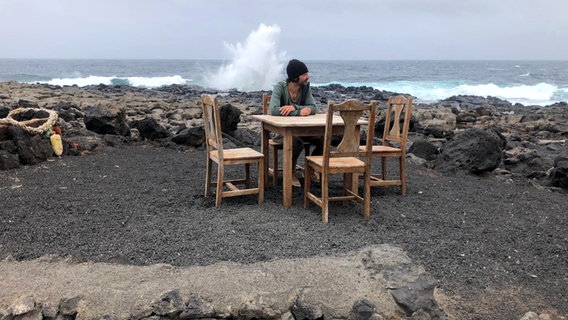 Schriftsteller Moritz Rinke sitzt auf einem Tisch am Meer auf Lanzarote, dahinter Felsen und Gischt © Moritz Rinke Foto: Moritz Rinke