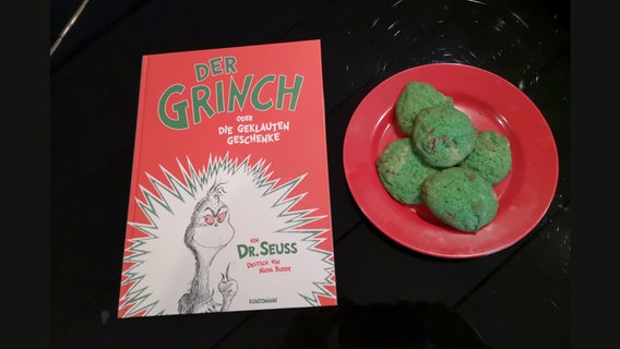 Das Buch "Der Grinch" von Dr. Seuss neben grünen Keksen auf einem roten Teller - Folge 49 von eat.READ.sleep © NDR Foto: Dennis Pfennig