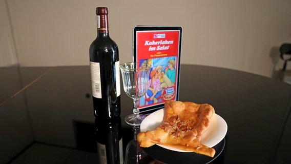Eine Flasche Rotwein neben einem Teller mit einem Stück weißer Pizza - Folge 62 von eat.READ.sleep © NDR 