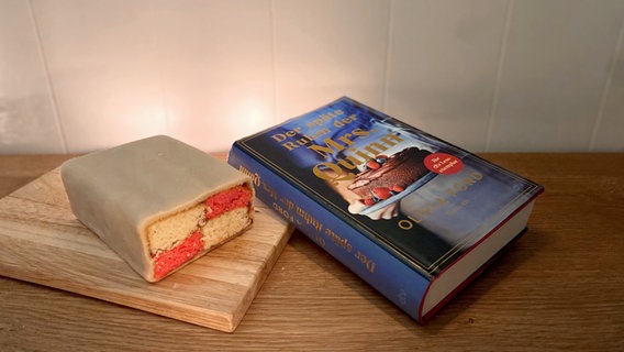 Ein Brett mit einem eckigen Kuchen in zwei Farben und einem Buch -  Folgenfoto von eat.READ.sleep © NDR Foto: Katharina Mahrenholtz