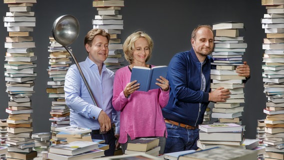 Die Hosts von eat.READ.sleep: Jan Ehlert (von links, mit einer riesigen Suppenkelle), Katharina Mahrenholtz (mit Buch) und Daniel Kaiser (angelehnt schlummernd an einen Bücherstapel) © NDR / Christian Spielmann Foto: Christian Spielmann