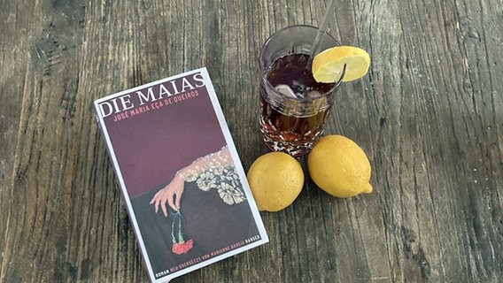 Ein Buchcover mit dem Titel "Die Maias" daneben ein gefülltes Glas und zwei Zitronen auf einem Holztisch. © NDR Foto: Daniel Kaiser
