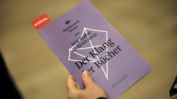 Der Bücherpodcast eat.READ.sleep. im Kleinen Saal der Elbphilharmonie: Eine Hand hält das Programmheft des Abends. © NDR Foto: Sebastian Fuchs